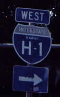 Marker pointing to west H-1, on cutout Interstate shield with state name and hyphenated route number