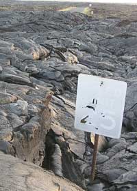 'Speed limit 25' sign with damaged surface sticks out of several feet of solid lava; small patch of yet-to-be-covered pavement in the background