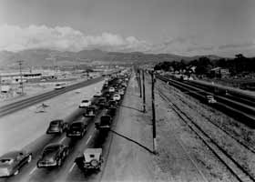 1951 black-and-white photo, of six-lane divided Kamehameha Highway to left of telephone poles and train track, with four-lane undivided Nimitz Highway to the right