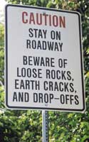 Warning sign: 'Caution | Stay on | roadway | Beware of | loose rocks, | earth cracks, | and drop-offs'