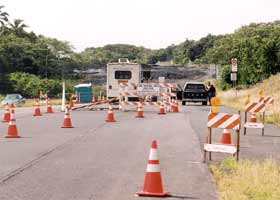 Wide view of tollbooth for lava viewing road, with trailer on left and sawhorses and orange cones narrowing two lanes of pavement to one approaching booth