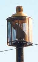 Civil defense siren, one horn in screened yellow enclosure pointing downward, with slanting deflector to direct sound outward