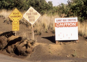 Three warning signs: 'Road Narrows | Proceed With Caution'; 'Use Your Four-Wheel Drive'; and 'Summit Road Conditions: CAUTION | Road Open to All Observatories'