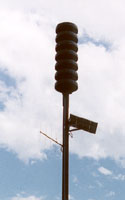 Civil defense sirens, seven green flat horns stacked vertically on a single pole