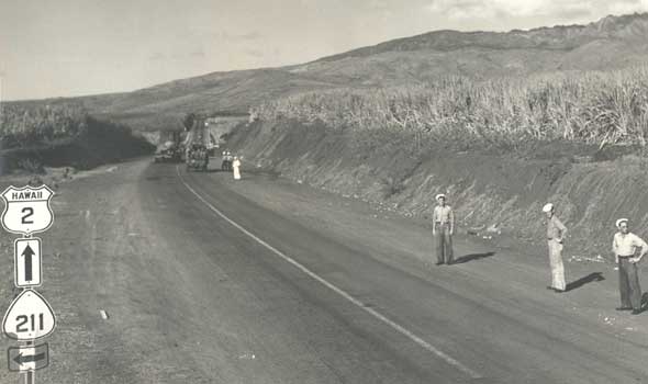 Primary and secondary route markers for wartime route system on Oahu, alongside road with sailors standing alongside and trucks in the background